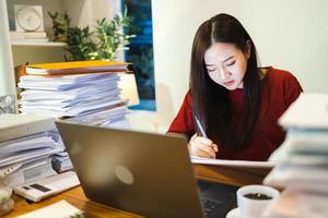 Workaholic people. Asian Woman check reports by computer laptop during overtime at home photo