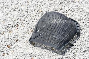The bucket is made of used black plastic. Placed on a pile of rocks. There is a bright light in the outdoors. photo