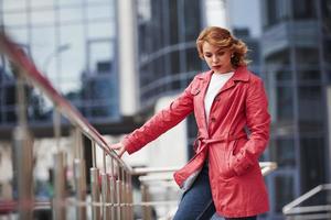 sujetando por barandillas. mujer bonita adulta con un cálido abrigo rojo camina por la ciudad los fines de semana foto