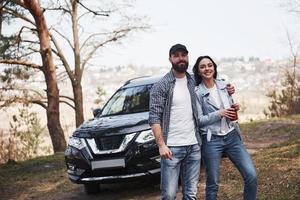 Embracing and enjoying the nature. Couple have arrived to the forest on their brand new black car photo