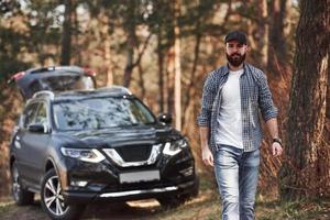 Alone in the woods. Bearded man near his brand new black car in the forest. Vacations concept photo