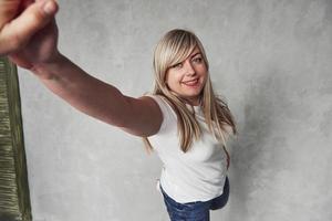 Reaching the hand of photographer. Young white woman in the studio standing against grey background photo