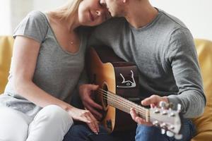 Gorgeous people. Playing on acoustic guitar for the girlfriend in the living room of new house photo