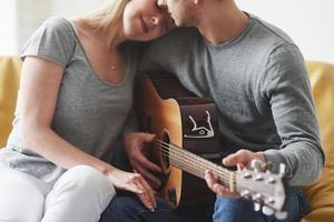 Gorgeous people. Playing on acoustic guitar for the girlfriend in the living room of new house photo