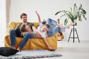 Hands on the sides like a plane. Happy family have fun on the yellow sofa in the living room of their new house photo