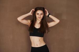 Ready for the fitness exercises. Young beautiful woman standing in the studio against brown background photo