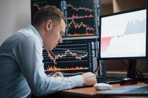 Doing his daily job. Man working online in the office with multiple computer screens in index charts photo