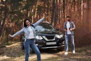 sacando un poco de café. disfrutando de la naturaleza. una pareja ha llegado al bosque en su nuevo auto negro foto