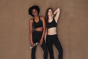 Toothy smile. Two multi ethnic female friends stands in the studio with brown background photo