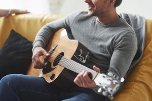 Man with acoustic guitar playing when sitting on the yellow sofa photo