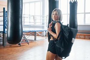 Looks back. Adult female with black bag and headphones in the training gym photo