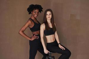 Taking a break. Two multi ethnic female friends stands in the studio with brown background photo