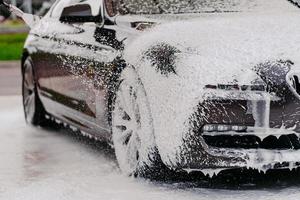 detergente quimico para limpieza de auto. coche en espuma blanca. vehículo de lavado. lavado de autos transporte cubierto con jabón. agua a alta presion foto