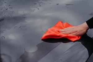 Mans hand cleans surface of black car with microfiber cloth. Maintenance and car wash concept. Professional cleaning. Selective focus photo