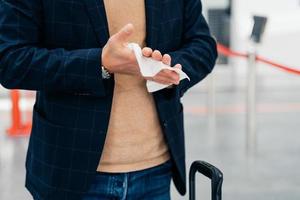 Keep your hands clean. Cropped shot of unrecognizable man disinfects hands with antibacterial napkin or antiseptic wet wipe during coronavirus spread, prevents virus, wants to be safe poses in airport photo