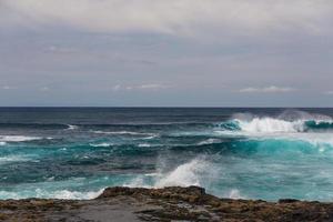 Turbulent ocean waves with white foam beat coastal stones photo