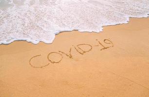 Closeup image of sea waves washing the word covid-19 from the sand on the beach. End of pandemic concept photo