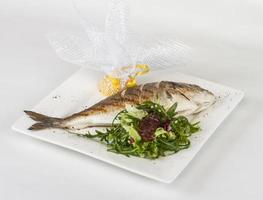 Dorada fish with salad on the white plate. Studio shot photo