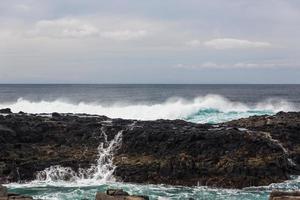 Turbulent ocean waves with white foam beat coastal stones photo