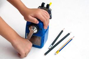 A boy is sharpening his pencil using mechanical sharpener over white background photo