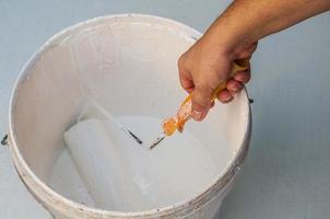 Hand holding rolling paint brush putting into white color bucket, construction painting work photo