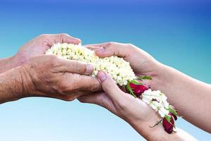 Young hands give jasmine garland to the older over light blue gradient background. Thai tradition for any special family occasions for paying high respective with love and care. photo