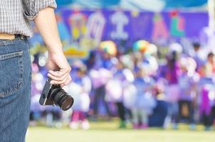 gente sosteniendo la cámara con personas borrosas abarrotadas en el día del deporte al aire libre animando la competencia-fotógrafo en el concepto de evento deportivo foto