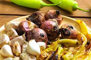 Vintage color tone of grilled garlic green spicy pepper and red onion putting in wooden plate on wooden floor prepared for chili paste cooking in Thai style. photo