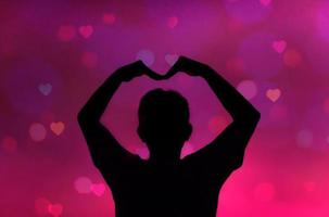 Silhouette of man making heart shape on pink background with heart bokeh photo