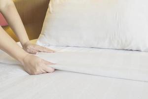 Lady hands set up white bed sheet in hotel room photo