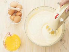 Lady's hand preparing cake using hand mixing machine with egg and butter photo