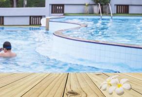 Blur of a boy in a swimming pool with white wood terrace and twin white plumeria flower photo