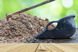 White wooden terrace with hoe and clam-shell shaped bucket and soil mound over green bokeh background photo