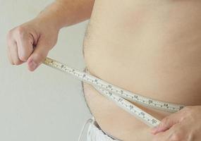 un hombre aprieta la cinta métrica alrededor de su vientre gordo, concepto de obesidad foto