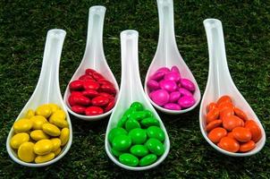 Colorful chocolate candy served on spoons with green grass background photo