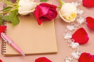 Red and white roses with small heart on book and pen photo