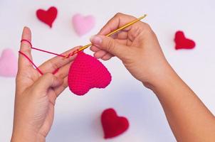 Lady's hands doing crochet work making red heart shape photo