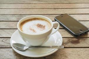 Coffee cup with mobile phone over brown plank wood table photo