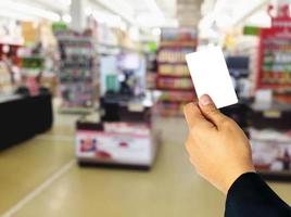 Businessman holding empty white card overlay on blurred superstore. photo