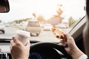 Man eating pizza and coffee while driving car dangerously photo