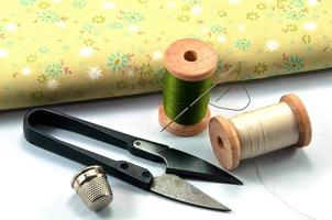 Dedal,aguja,carretes y tijera con tela para coser sobre fondo blanco. foto