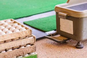 Closeup of old golf ball in wooden box container and soft focus of golf ball dispenser. Photo taken in drive golf practice club, Thailand