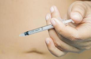 A lady is injecting insulin into her stomach. Photo is focus at syringe.