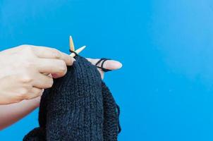 Woman's hands is making black hat knitting over light blue background photo