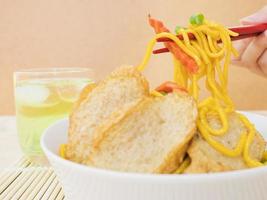 yakisoba con vaso de té verde frío sobre almohadilla de bambú con palillos y mano foto