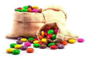 Caramelos de chocolate coloridos en mini bolsa de saco sobre fondo blanco. foto