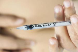 A lady is injecting insulin into her stomach. Photo is focus at syringe.