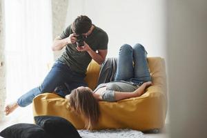 equipo profesional. fotógrafo tomando una foto de una joven que yacía en el sofá blanco