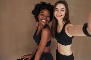 Capturing the moment. Two multi ethnic female friends stands in the studio with brown background photo