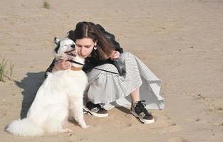 mujer joven abrazando a su perro mientras se sienta en una playa de mar. otoño caminando y pasando tiempo con mascotas. amor y afecto, amistad y unión. foto